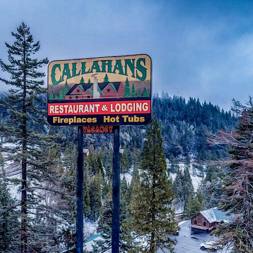 A sign for Callahan's Restaurant & Lodging in a snowy, wooded area mentions fireplaces and hot tubs. Mountains and cabins are visible in the background.