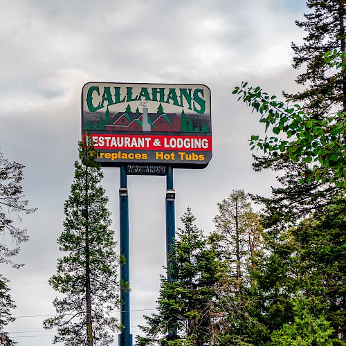 A tall sign among trees reads "Callahans Restaurant & Lodging - Fireplaces - Hot Tub" with a cloudy sky in the background.