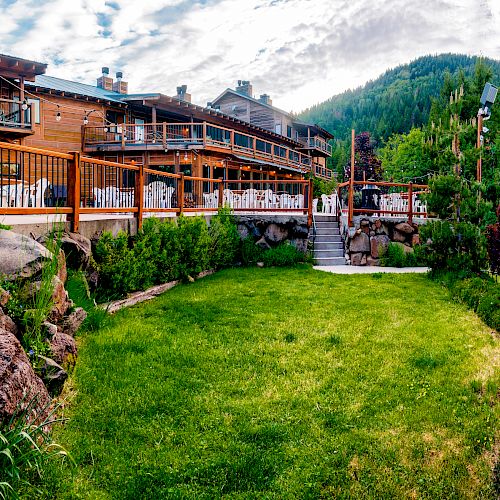A beautiful lodge with outdoor seating and lush gardens backed by a scenic mountainous landscape, surrounded by green trees and colorful foliage.