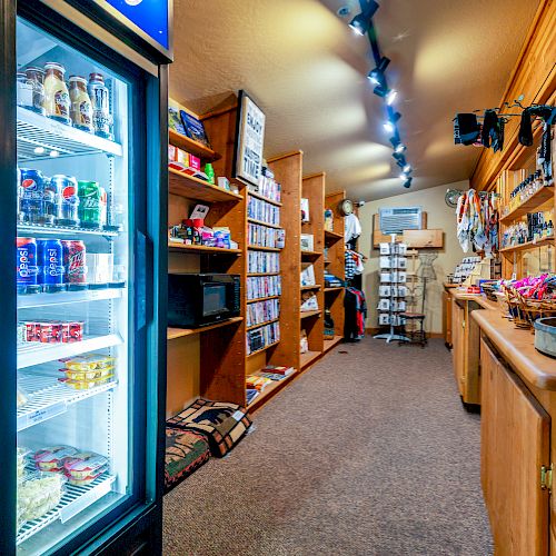 The image shows the interior of a small convenience store or gift shop with shelves of various goods, snacks, beverages, and refrigerators on the left.