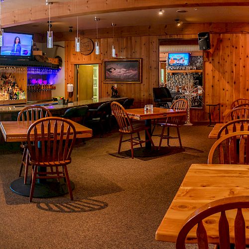 The image depicts an empty restaurant or bar with wooden furniture, a television on the wall, and a visible bar area with various bottles and lighting.