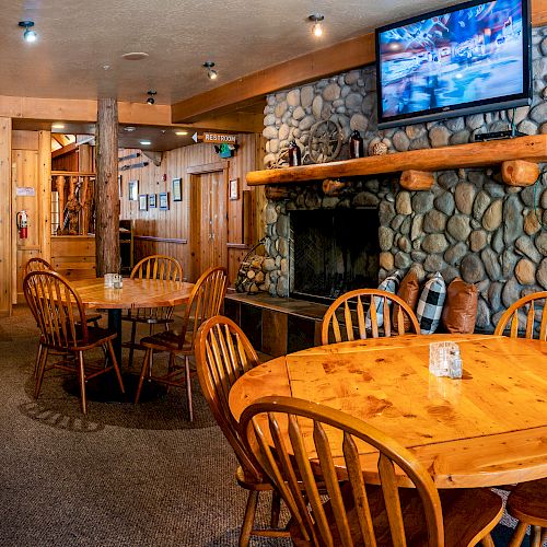 A cozy restaurant with wooden tables and chairs, a stone fireplace, and a TV mounted above it displaying a scenic image.