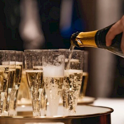 A person is pouring champagne into several glasses arranged on a gold tray.