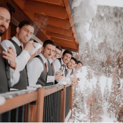 A group of men in formal attire, some smoking cigars, are standing on a snowy balcony with snowy mountains in the background.