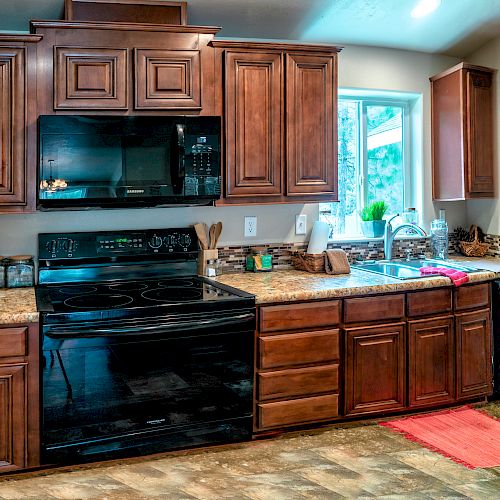 A kitchen with wooden cabinets, black appliances including a stove and microwave, a sink under a window, and various small appliances on the counter.