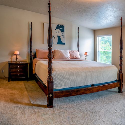 A bedroom with a four-poster bed, two nightstands with lamps, wall art above the bed, and a cluster of circular decorations on the right wall.