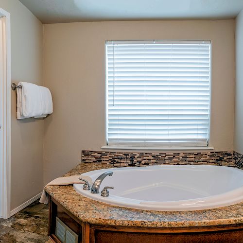 The image shows a bathroom with a large bathtub, a window with blinds, and a shower and toilet in the adjacent room.