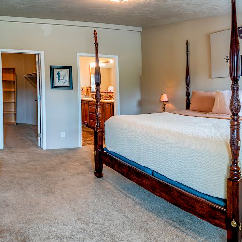 This image shows a cozy bedroom with a large four-poster bed, wooden furniture, a closet, and an entrance to a bathroom.