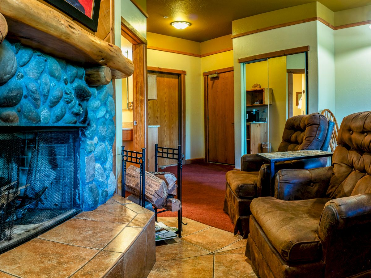 The image depicts a cozy living room with a stone fireplace, two brown reclining chairs, and warm lighting fixtures.