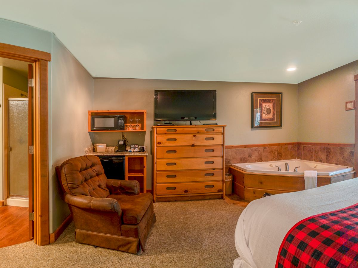 This image depicts a cozy bedroom with a bed, recliner, dresser with TV, a Jacuzzi, kitchenette, and attached bathroom, ending the sentence.