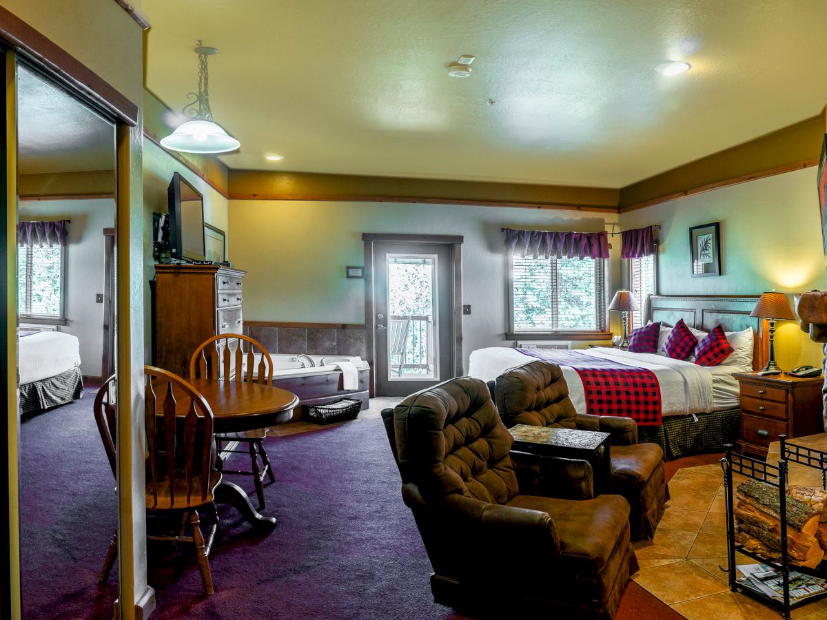 A cozy room with a king bed, a round dining table, lounge chairs, a TV, mirrored closet doors, purple carpet, and large windows letting in natural light.