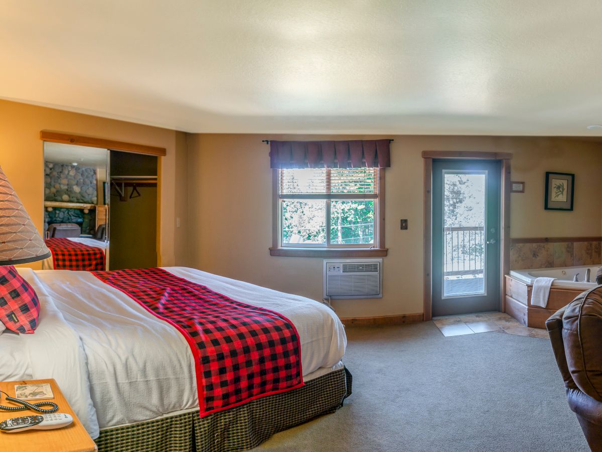 A cozy bedroom with a double bed, checkered decor, a window with a view, and a jacuzzi tub in the corner. A chair sits near the bed.