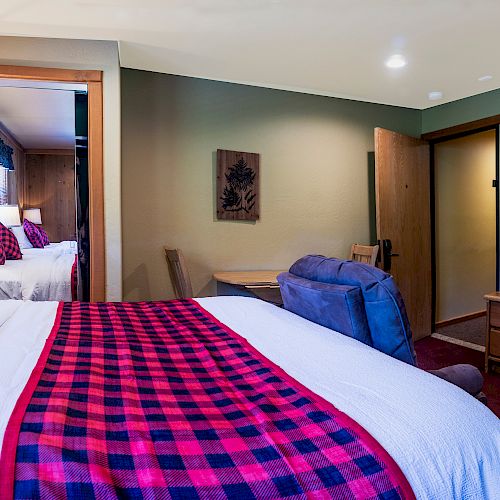 A cozy bedroom with plaid red and black bedding, wooden furniture, a TV, and wall art. The room is well-lit, with natural and artificial lighting.