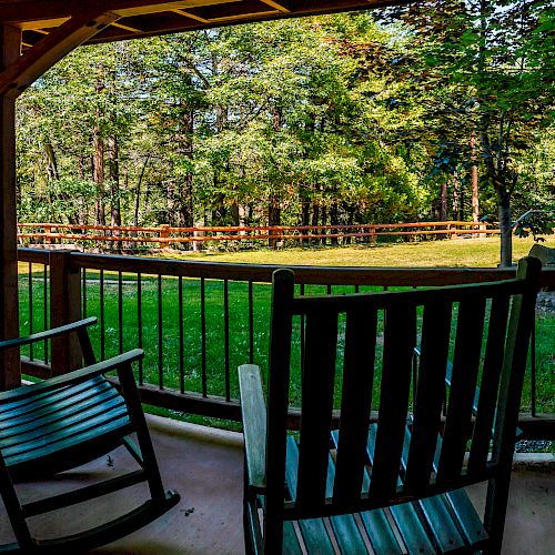 A covered porch with wooden rocking chairs overlooks a grassy yard and dense trees, creating a serene and relaxing outdoor space.