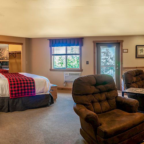 A cozy bedroom features a bed, two armchairs, a chest of drawers, a TV, and a door leading outside, creating a comfortable setting.