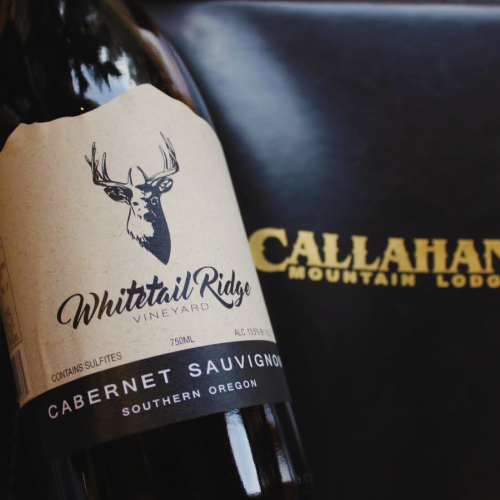 A bottle of Whitetail Ridge Cabernet Sauvignon from Southern Oregon is placed beside a Callahan's Mountain Lodge menu or brochure.