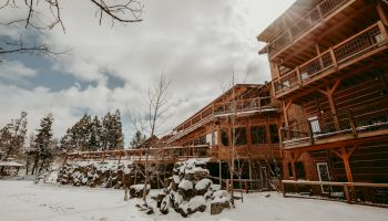 A snowy scene with a wooden lodge surrounded by trees under a cloudy sky, showcasing winter serenity.
