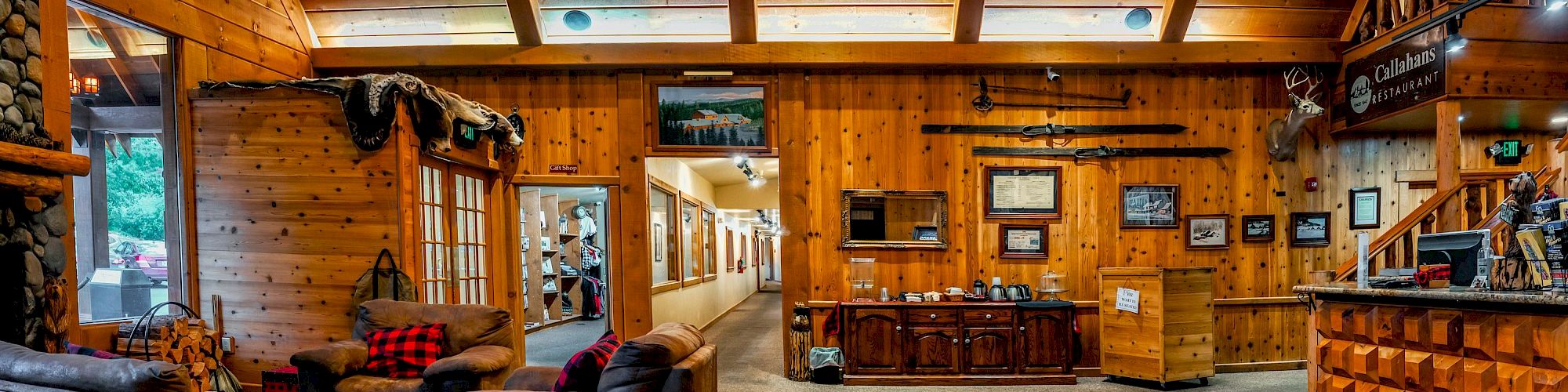 A cozy, rustic lodge interior with wooden walls, leather sofas, mounted animal heads, a chandelier, and various decorations.