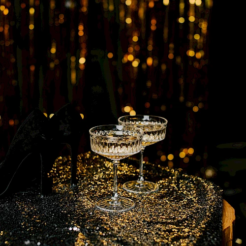 Champagne flutes glisten on a sequined table as warm fairy lights glow in the background, creating a festive, glamorous atmosphere.
