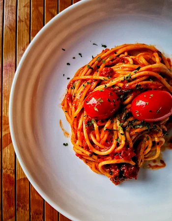 Spaghetti with tomato sauce, cherry tomatoes, herbs, and olive oil on a white plate, served on a wooden table, deliciously plated.