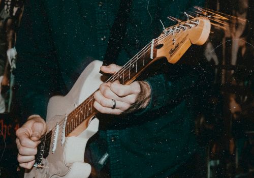 A guitarist&rsquo;s hands playing an electric guitar, fingers on the strings while bright light streaks cross the scene.