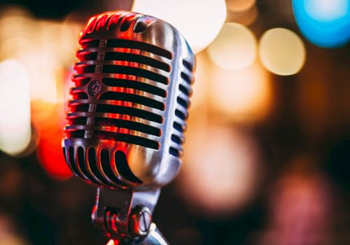 A close-up of a vintage-style microphone with red lighting and soft bokeh lights behind it, ready to capture vocals.