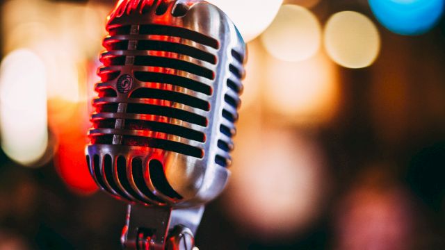 A close-up of a vintage-style microphone with red lighting and soft bokeh lights behind it, ready to capture vocals.