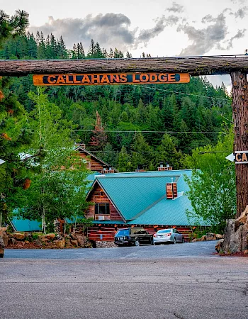 A rustic gateway labeled Callahan’s Lodge arches over a forest road, with cars and signs pointing the way into the lodge.