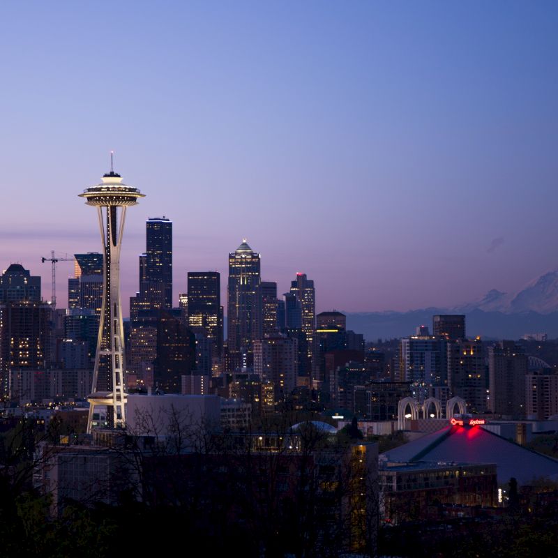 This image features a cityscape with the iconic Space Needle, numerous skyscrapers, and a distant mountain under a twilight sky.