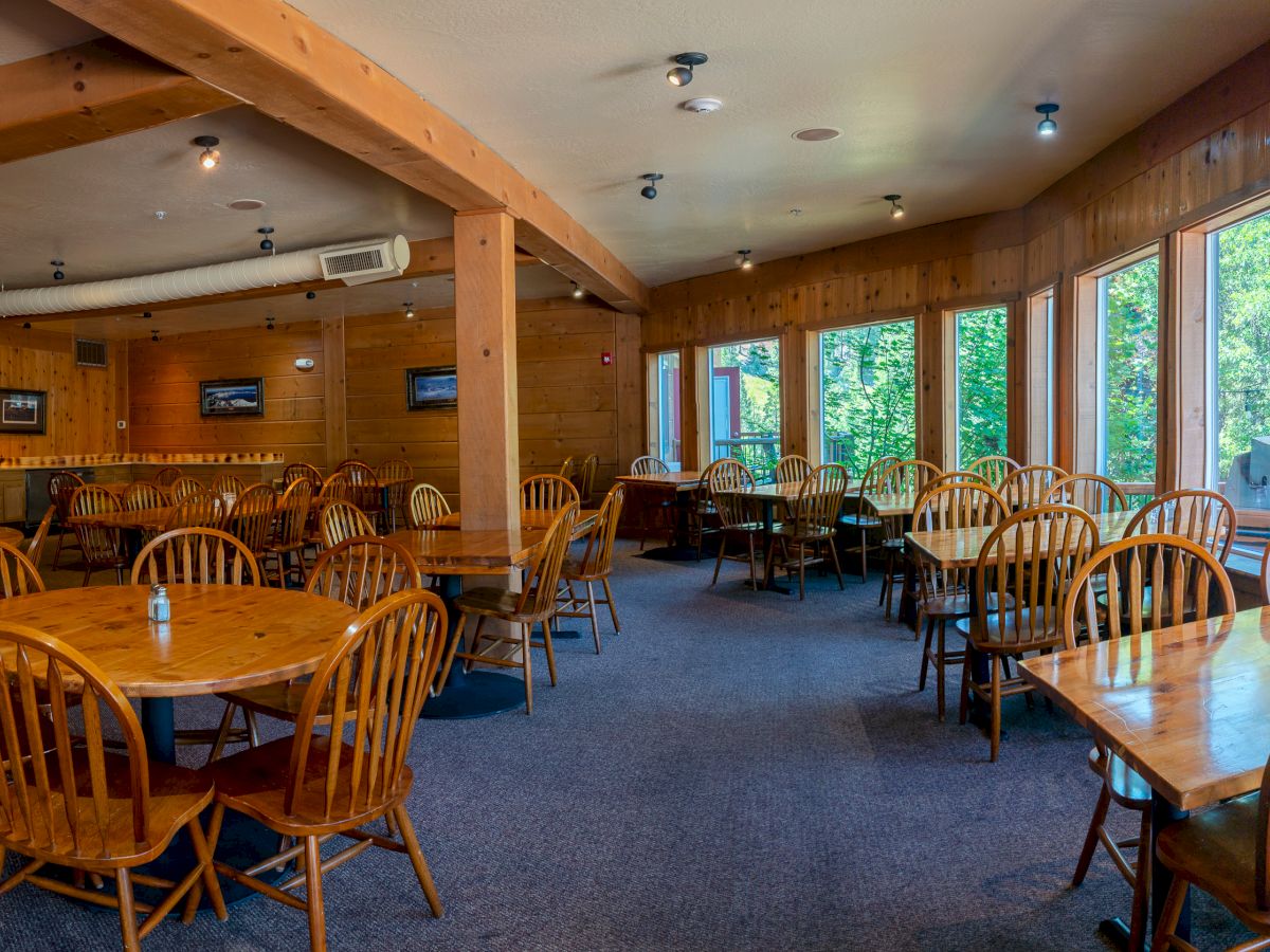 The image shows a cozy restaurant with wooden tables and chairs, large windows, and plenty of natural light entering the room.